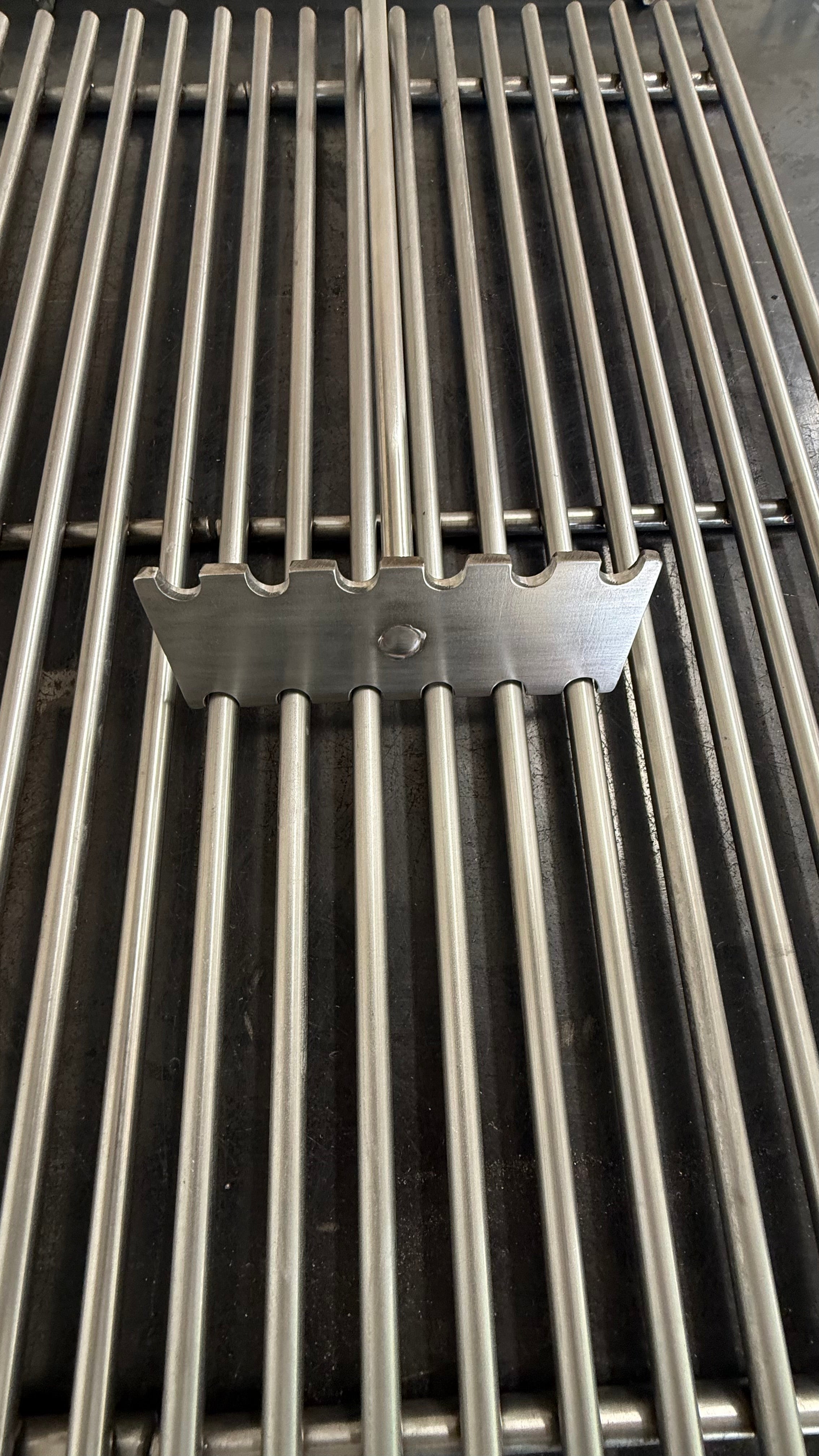 Notched stainless steel grate cleaner seated on a round bar BBQ cook grate